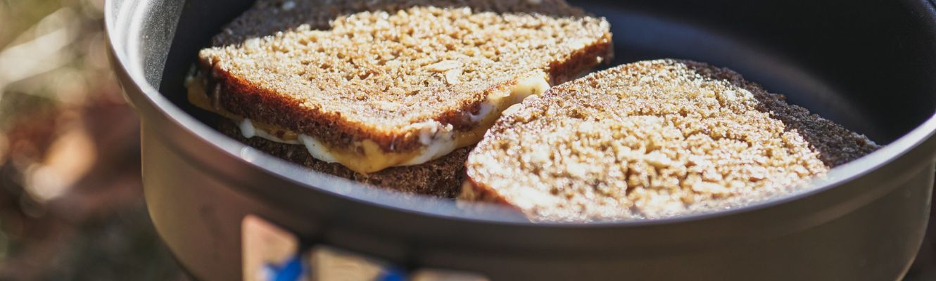 Two grilled cheese sandwiches cooking in a black camping pan